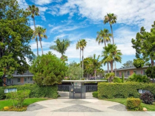 front gate and driveway to the apartments surrounded by trees, grass and a hedge