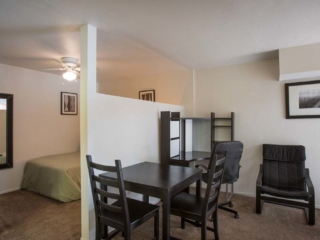 Apartment interior showing the bedroom on the left with a wall divider then the dining table and office area on the right