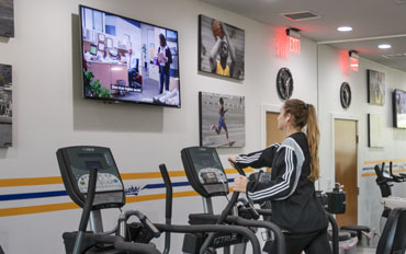 Woman on an elliptical in the gym watching the tv